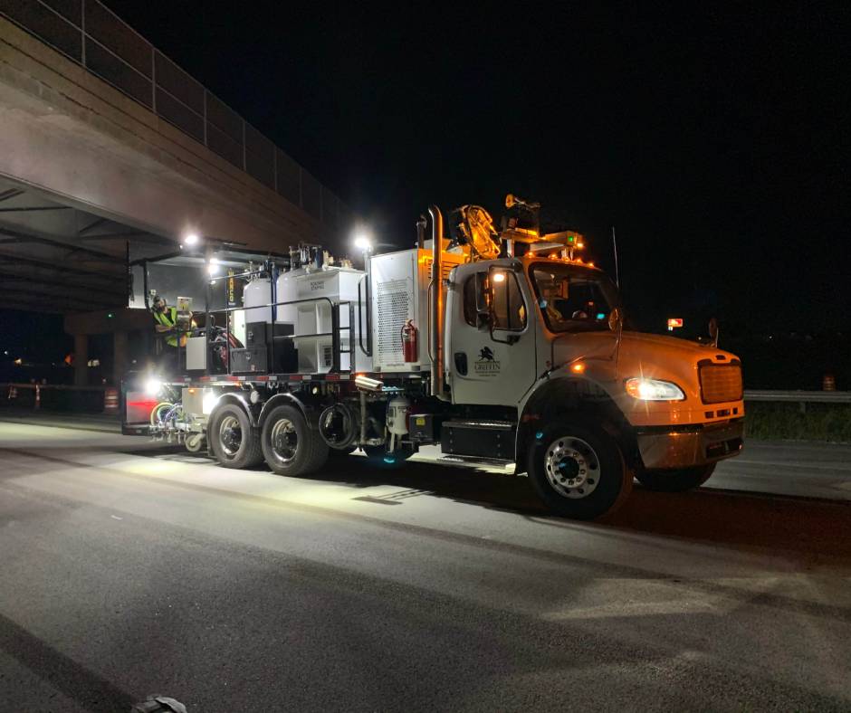 A pavement marking truck working on a highway at night with bright lights shining.