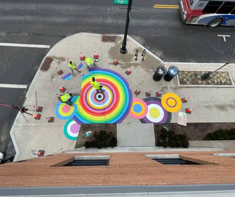 An ariel view of a corner sidewalk with multi-colored preformed marking tape designs.