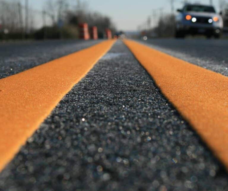 A close-up picture of a black asphalt road with orange thermoplastic pavement marking.